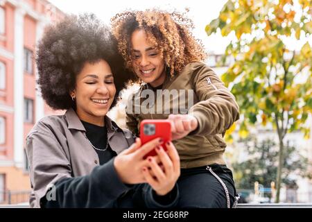 Photo de filles fraîches afro souriant et utilisant le téléphone dans la rue. Banque D'Images