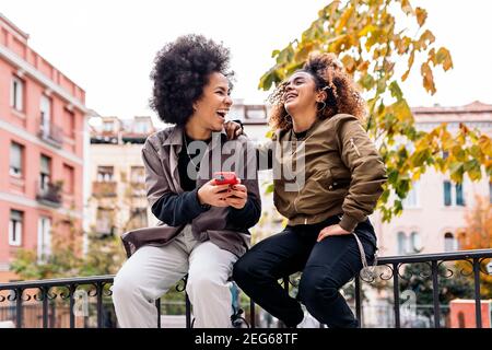 Photo de filles fraîches afro souriant et utilisant le téléphone dans la rue. Banque D'Images