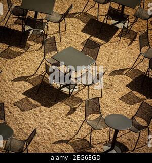 Terrasse de café vide avec tables et chaises projetant des ombres sur une surface sablonneuse en plein soleil France Banque D'Images