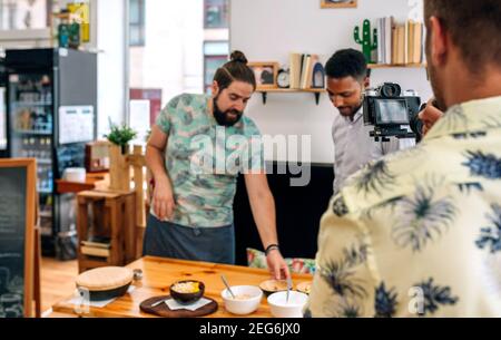Chef cuisinier caméraman qui explique pendant un spectacle de cuisine. Mise au point sélective sur l'appareil photo au premier plan Banque D'Images