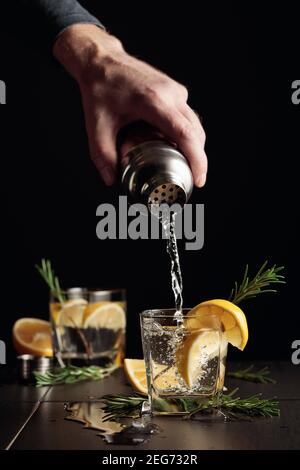 Cocktail Gin et Tonic avec citron et romarin sur fond noir. Banque D'Images