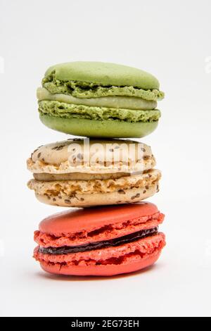 Trois macarons vibrants sont magnifiquement disposés dans une pile, mettant en valeur leurs couleurs et textures distinctes. Les friandises vertes, beiges et rouges se démarquent Banque D'Images