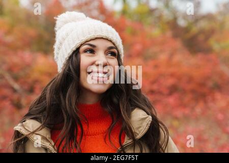 Belle brunette heureuse femme en tricot chapeau souriant tout en se promenant en forêt d'automne Banque D'Images