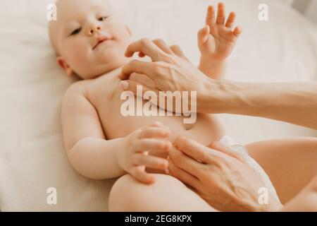 Massage de bébé, maman massage le ventre de bébé pendant la colique, nouveau-né avec colique couché sur son dos sans vêtements, la main de mère sur son ventre l'aide Banque D'Images