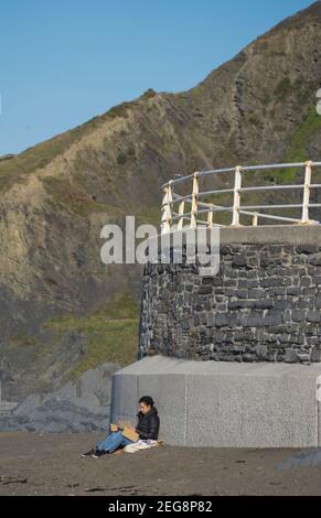 Femme lisant et appréciant le soleil à la promenade de la plage du Nord, Aberystwyth, Ceredigion, pays de Galles, Royaume-Uni Banque D'Images