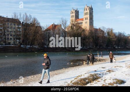 Munich, Allemagne - 13 février 2021 : l'homme marche avec son téléphone portable à côté de l'église St Maximilian depuis le front d'eau de l'Isar. Les gens qui marchent le long Banque D'Images