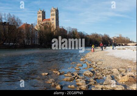 Munich, Allemagne - 13 février 2021 : vue sur l'église St Maximilian depuis le front de mer de l'Isar. Les gens qui marchent le long de l'esplanade en profitant du soleil Banque D'Images