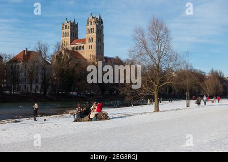Munich, Allemagne - 13 février 2021 : vue sur l'église St Maximilian depuis le front de mer de l'Isar. Les gens qui marchent le long de l'esplanade en profitant du soleil Banque D'Images