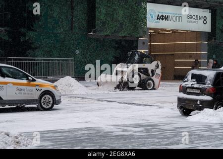 Moscou. Russie. 12 février 2021. Une petite pelle hydraulique avec un godet élimine la neige d'une route dans une rue urbaine lors d'une forte chute de neige. Hiver Banque D'Images