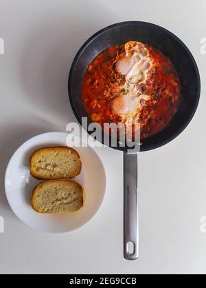 Shakshuka de tomate avec deux œufs sur la poêle et du pain plaque blanche Banque D'Images