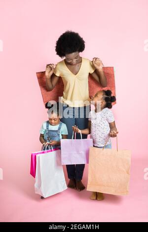 Belle jeune mère africaine et deux petites filles mignonnes en tenue décontractée, se tenant satisfait des sacs de shopping dans les mains, faisant des achats à Banque D'Images