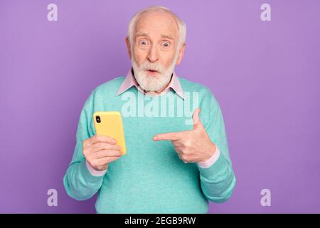 Photo portrait de l'homme senior montrant le téléphone portable surpris conseil dans vêtements sarcelle isolés sur fond violet pastel Banque D'Images