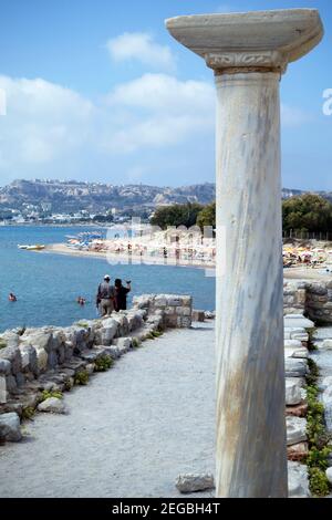 Un pilier en marbre des ruines d'Agios Stefanos contraste avec les touristes, les parasols et les baigneurs de soleil sur la plage de Kefalos, Kos Banque D'Images