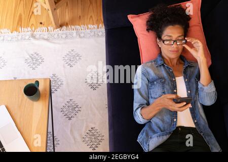 Femme caucasienne couchée sur un canapé avec un smartphone, se détendant à la maison Banque D'Images