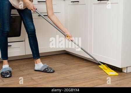 Une femme lave le chauffage au sol dans sa maison. Nettoyez la saleté sous le meuble de cuisine. Banque D'Images