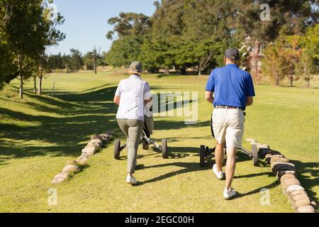 Homme et femme caucasien de haut niveau marchant à travers la tenue de parcours de golf sacs de golf Banque D'Images