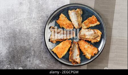 Filet de poisson frit à la goberge (merlu) sur une assiette ronde sur fond gris foncé. Vue de dessus, plan d'appartement Banque D'Images