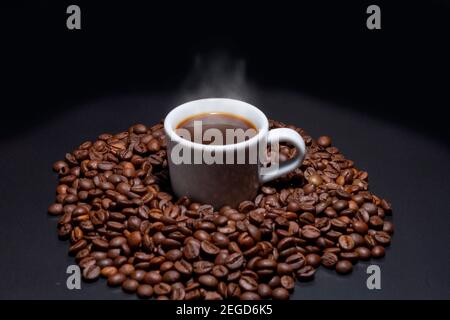 Tasse de café blanc avec une boisson à l'intérieur et entourée de grains de café torréfiés de la variété Robusta. Banque D'Images