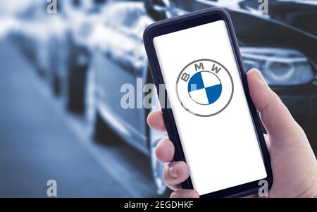 Galice, Espagne; janvier 09 2021: Main tenant un smartphone avec le nouveau logo BMW à l'écran et des voitures floues en arrière-plan. Copier l'espace Banque D'Images