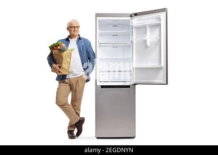 Portrait complet d'un homme mûr penché sur un ouvrez le réfrigérateur vide et tenez un sac d'épicerie isolé arrière-plan blanc Banque D'Images