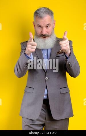 Studio portrait homme d'affaires mûr vêtu de points gris costume sur l'appareil photo, je vous choisis concept, fond jaune Banque D'Images