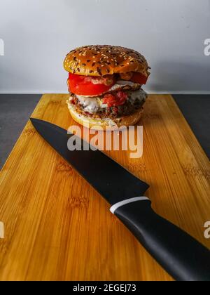 Hamburger avec un rouleau de fromage au bacon de tomate de sésame à la fin de bois avec couteau de chef noir Banque D'Images