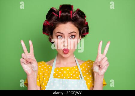 Photo de belle fille faire v-signe envoyer air baiser elle les mains dans la farine de blé portent des rouleaux de cheveux de t-shirt à pointillés jaunes isolé sur la couleur verte Banque D'Images