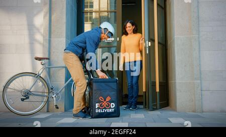 Happy Food Delivery un homme portant un sac à dos thermique sur un vélo livre la commande du restaurant à une cliente heureuse. Le service de messagerie livre le déjeuner à emporter Banque D'Images