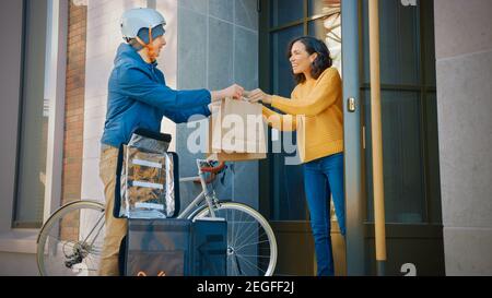 Happy Food Delivery un homme portant un sac à dos thermique sur un vélo livre la commande de restaurant à une belle cliente féminine. Le service de messagerie livre un déjeuner à emporter Banque D'Images