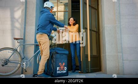 Happy Food Delivery un homme portant un sac à dos thermique sur un vélo livre la commande du restaurant à une belle cliente féminine. Le service de messagerie livre le déjeuner à emporter Banque D'Images