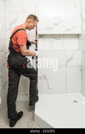 L'ouvrier installe un profil métallique de la cabine de douche avec un tournevis. Banque D'Images