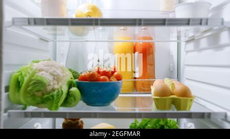 Point de vue POV prise de vue du réfrigérateur de cuisine. Réfrigérateur éclairé et plein de bons aliments: Tomates cerises, oeufs, jus frais et chou, chou-fleur. Banque D'Images