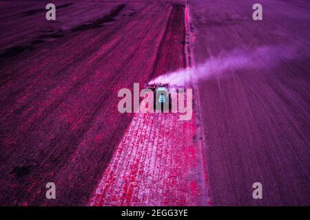 Un tracteur travaille dans un champ pour préparer la saison de plantation. Prendre une lumière infrarouge de fausses couleurs avec un filtre qui émule le film Kodak aérochrome. Banque D'Images