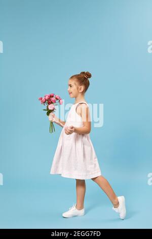 belle petite fille souriante tenant un bouquet de roses isolé sur fond de studio bleu. vue latérale Banque D'Images