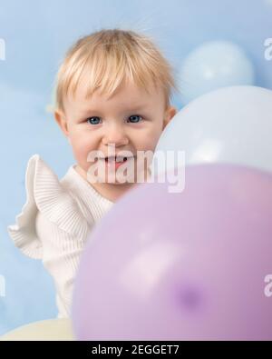 Belle petite fille gaie de 1 an avec des yeux bleus et deux dents dans un col de cygne blanc parmi les ballons et regarde la caméra Banque D'Images