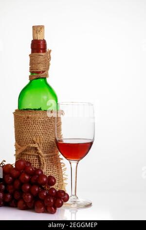 Verre de vin rouge avec raisins et bouteille sur fond blanc. Banque D'Images