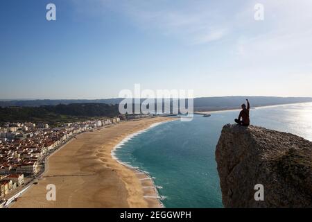 Concept de voyage pour la vie. L'homme est assis sur la falaise, en regardant d'en haut sur la plage et la petite ville. La main droite est relevée Banque D'Images