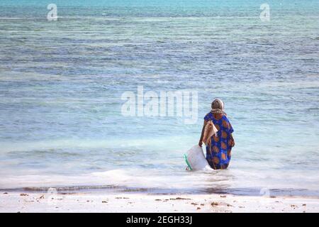 Silhouette de la femme locale zanzibar dans les vêtements musulmans traditionnels wade dans l'eau de mer, climat tropical. Zanzibar, Tanzanie Banque D'Images