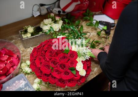 Fleuriste faisant boîte de fleurs avec des roses rouges et des fleurs blanches sur la table Banque D'Images