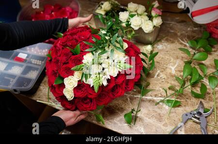 Fleuriste faisant boîte de fleurs avec des roses rouges et des fleurs blanches sur la table Banque D'Images