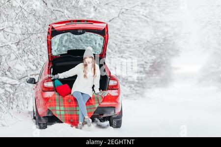 Une femme avec du café chaud dans ses mains est assise dans un voiture rouge par une journée d'hiver enneigée Banque D'Images