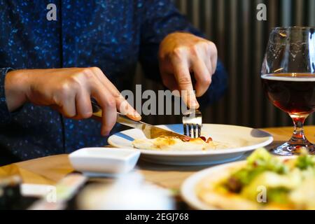 Le maillot BLEU DÉFIE la personne ET coupe la pizza dans le café. Un jeune homme affamé avec couteau et fourchette à couper et manger de la pizza au café au dîner Banque D'Images