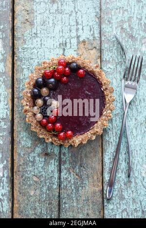 Tarte végétalienne crue avec confiture de baies et raisins de Corinthe biologiques vue du dessus de l'arrière-plan bleu Banque D'Images