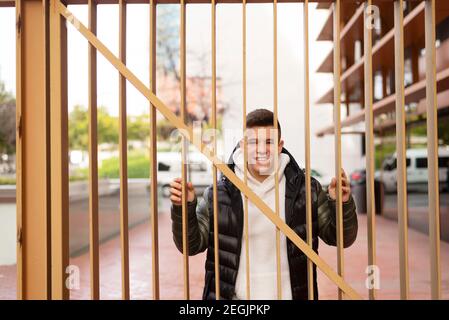 Jeune homme debout derrière une clôture en métal tout en regardant la caméra Banque D'Images