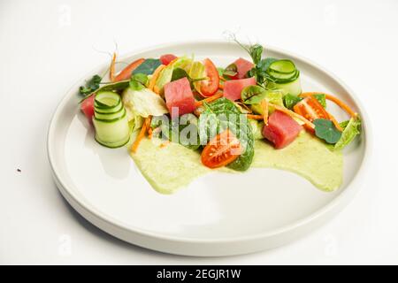 Salade de thon avec vinaigrette sur une assiette. Ingrédients laitue Iceberg, thon, tomates cerises, épinards, carottes, concombre, sauce de spécialité. Pour le menu du restaurant. Banque D'Images