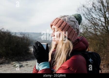 femme souriante tenant une boisson chaude tout en appréciant le froid Air au Royaume-Uni Banque D'Images