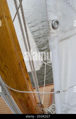 Détail d'une voile attachée au mât en bois d'un bateau à voile en cours d'afloat et sous la voile, naviguant au-dessus de l'eau grise.Œillets en tissu blanc, Banque D'Images