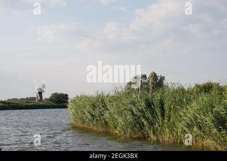 Un virage dans une rivière par un jour venteux : des lits reedbeds verts soufflant dans la brise, et un moulin à vent blanc (ou pompe à vent) sur la rive au loin.Norfolk Banque D'Images