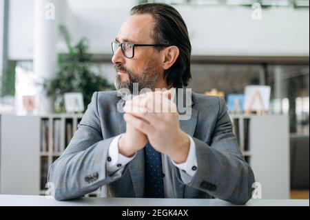 Portrait d'un homme d'affaires âgé pensif au bureau. Un homme d'affaires sérieux d'âge moyen est assis à son bureau, regarde loin, pensant à résoudre des problèmes de travail Banque D'Images