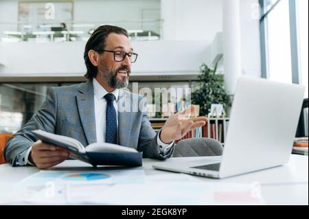 Homme influent et mature qui fait une réunion d'information en ligne avec des collègues, explique le nouveau plan d'affaires pour l'entreprise. Patron homme confiant discutant avec les employés Banque D'Images